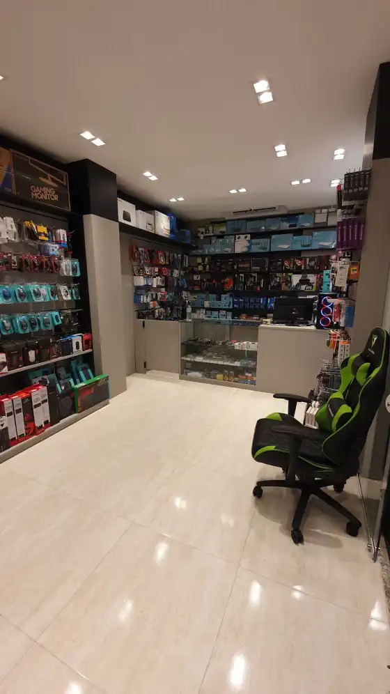 Dentro da loja: piso claro, paredes de caixas de produtos e a cadeira gamer verde e preta